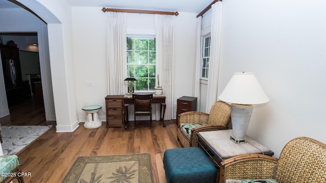living area with arched walkways, baseboards, and wood finished floors