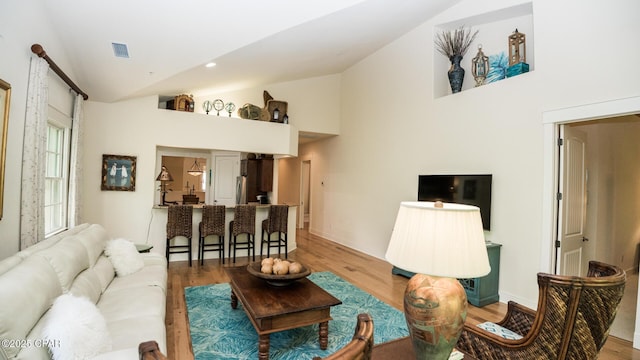 living area with visible vents, light wood finished floors, baseboards, and high vaulted ceiling