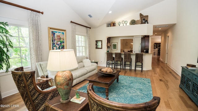 living room with baseboards, vaulted ceiling, light wood-style flooring, and visible vents