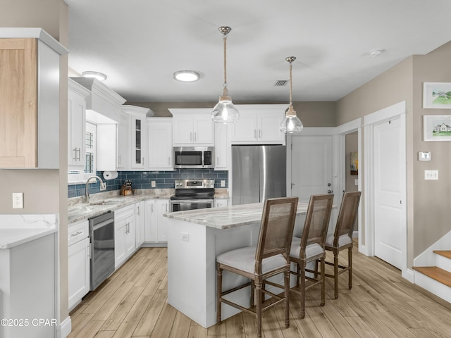kitchen featuring a sink, light wood-style flooring, a center island, white cabinets, and appliances with stainless steel finishes