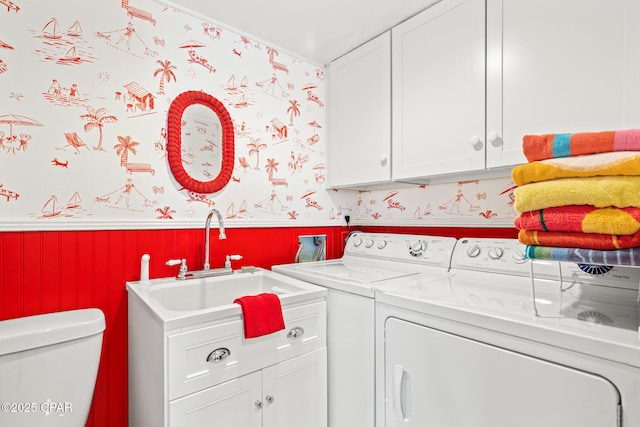 washroom with wainscoting, washing machine and dryer, cabinet space, a sink, and wallpapered walls