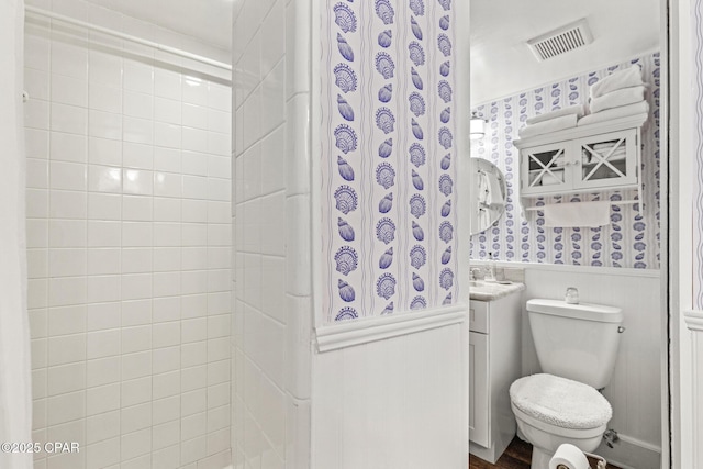 bathroom featuring visible vents, vanity, wainscoting, toilet, and wallpapered walls