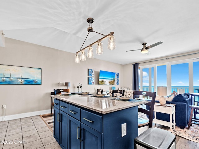 9860 S Thomas Dr Unit 1202, Panama City Beach, FL 32408 - kitchen with blue cabinetry, a ceiling fan, a kitchen island, light stone countertops, and a breakfast bar area
