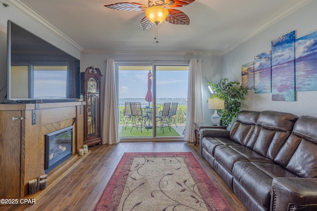 living area featuring ornamental molding, hardwood / wood-style flooring, a ceiling fan, and a glass covered fireplace