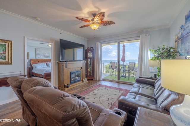 living room with ceiling fan, wood finished floors, ornamental molding, and a glass covered fireplace