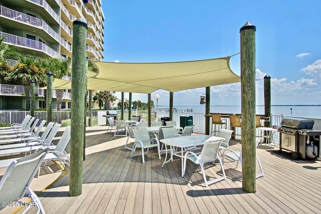wooden terrace with grilling area, outdoor dining space, and a water view