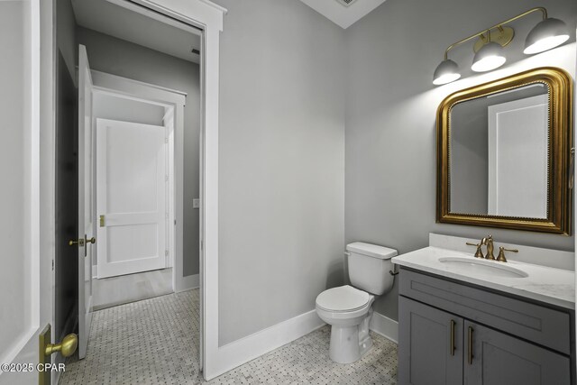 half bathroom with baseboards, toilet, and vanity