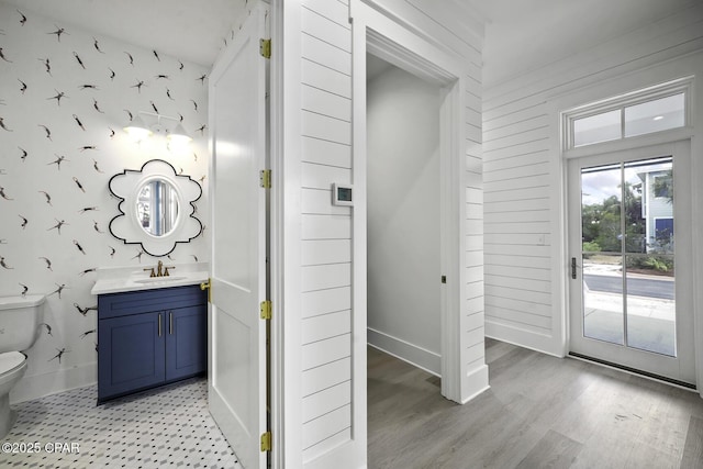 bathroom with baseboards, vanity, toilet, and wallpapered walls