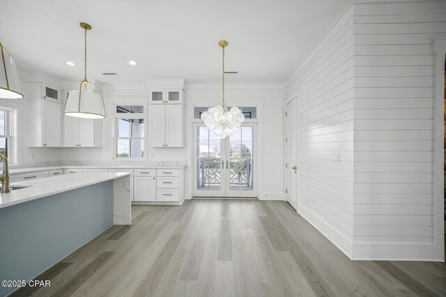 kitchen featuring light stone countertops, white cabinets, a notable chandelier, glass insert cabinets, and ornamental molding