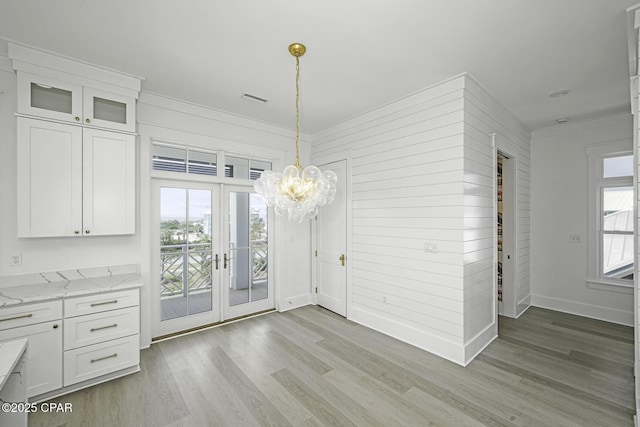unfurnished dining area featuring a notable chandelier, light wood finished floors, french doors, baseboards, and ornamental molding