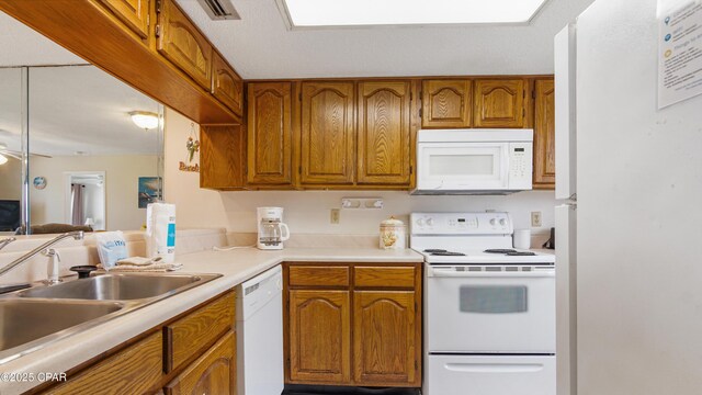 kitchen with a sink, light countertops, brown cabinetry, and white appliances