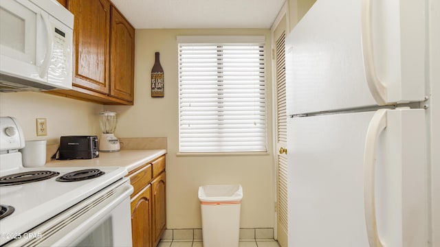 kitchen with light countertops, brown cabinets, light tile patterned floors, and white appliances