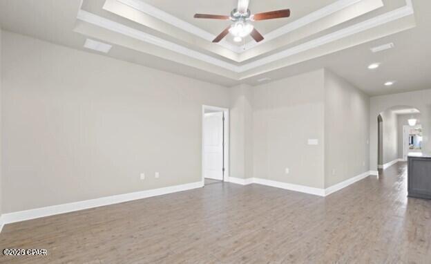 empty room with arched walkways, a raised ceiling, and ceiling fan