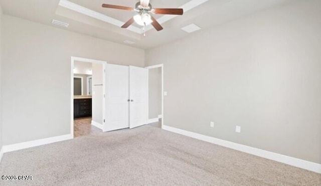 unfurnished bedroom with light colored carpet, a ceiling fan, baseboards, ensuite bathroom, and a tray ceiling