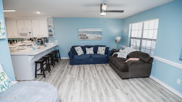 living area with baseboards, a ceiling fan, and light wood-style flooring