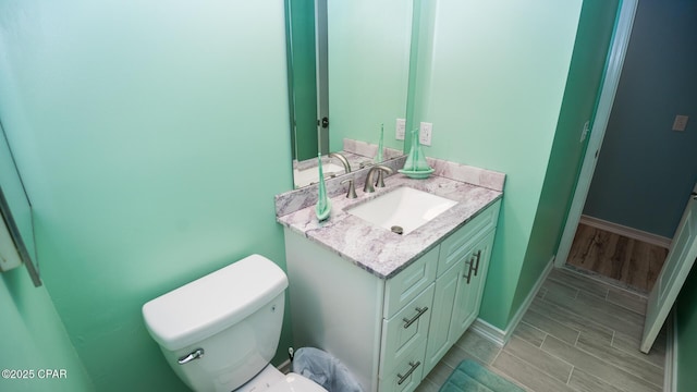 half bathroom with vanity, baseboards, wood tiled floor, and toilet