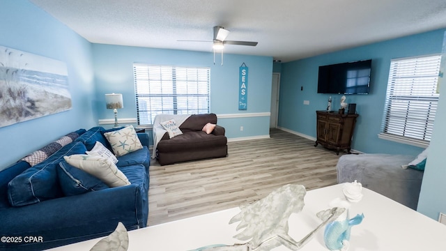 living area with plenty of natural light, a ceiling fan, baseboards, and wood finished floors