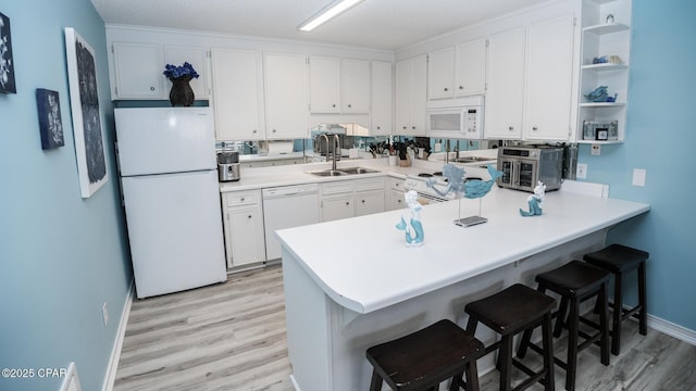 kitchen featuring a sink, baseboards, a peninsula, light wood-style floors, and white appliances