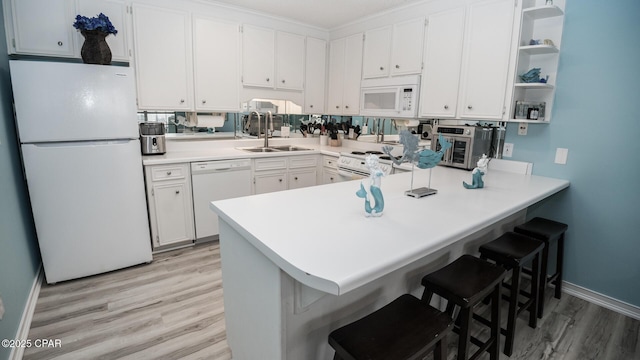 kitchen with a peninsula, white appliances, white cabinetry, a sink, and light wood-style flooring