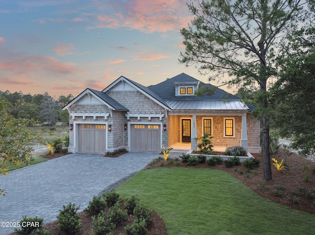 craftsman house featuring covered porch, metal roof, a garage, decorative driveway, and a front lawn