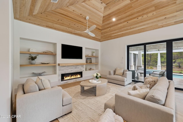 living area featuring high vaulted ceiling, built in shelves, a ceiling fan, wooden ceiling, and a lit fireplace