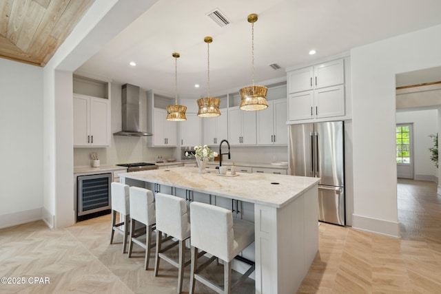 kitchen with visible vents, appliances with stainless steel finishes, baseboards, wine cooler, and wall chimney exhaust hood