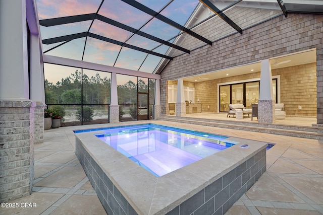 pool at dusk with a lanai, a patio, and an in ground hot tub