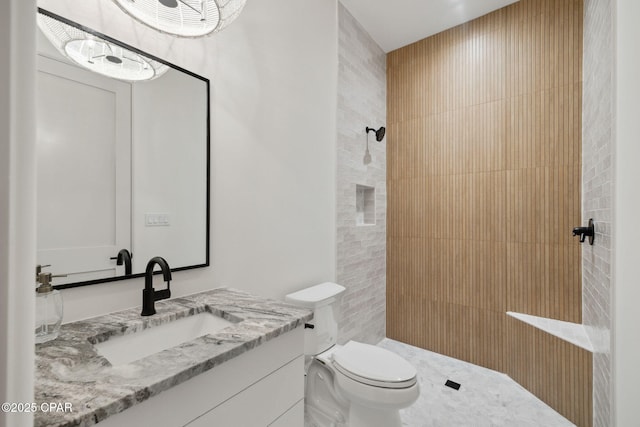 bathroom featuring vanity, a tile shower, and toilet