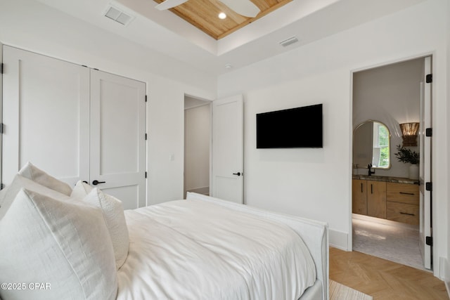bedroom featuring a tray ceiling, visible vents, ensuite bathroom, and a closet