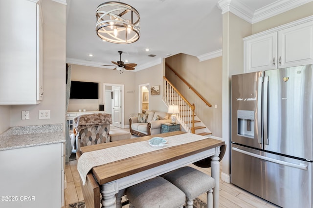 dining space with ornamental molding, stairway, light wood-type flooring, and ceiling fan with notable chandelier