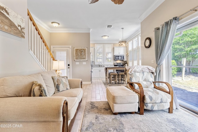 living room with stairs, visible vents, crown molding, a ceiling fan, and baseboards