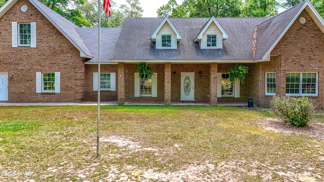 view of front of home with a shingled roof, a front lawn, and brick siding