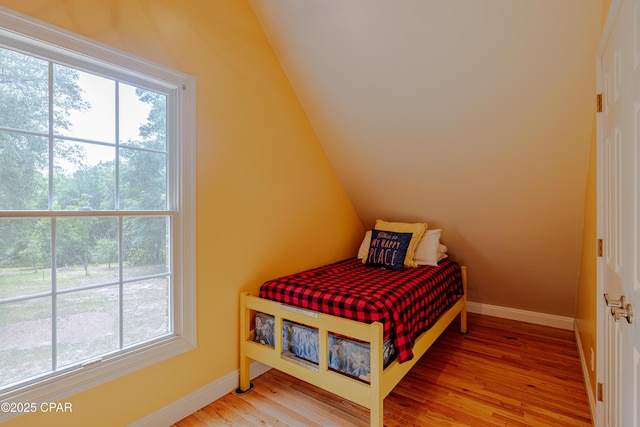 bedroom with baseboards, multiple windows, lofted ceiling, and light wood-style floors