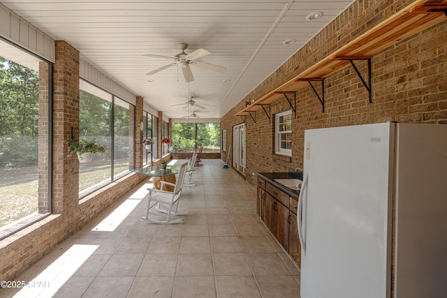 unfurnished sunroom with a sink, tile patterned floors, a ceiling fan, and brick wall