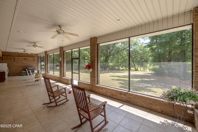 unfurnished sunroom featuring a ceiling fan, brick wall, and tile patterned flooring