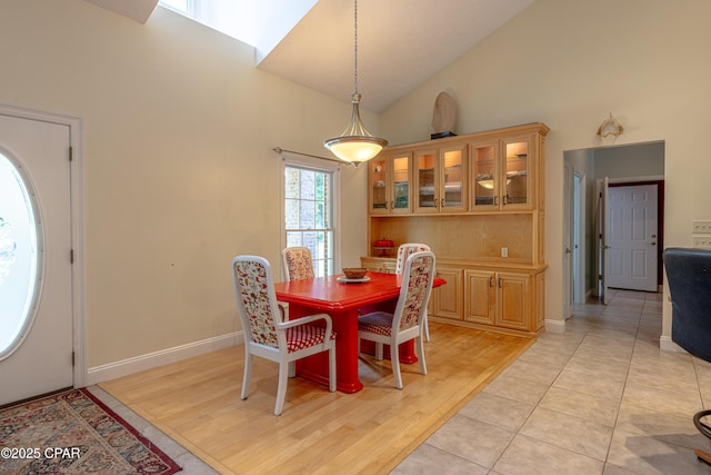 dining room featuring light tile patterned floors, high vaulted ceiling, and baseboards