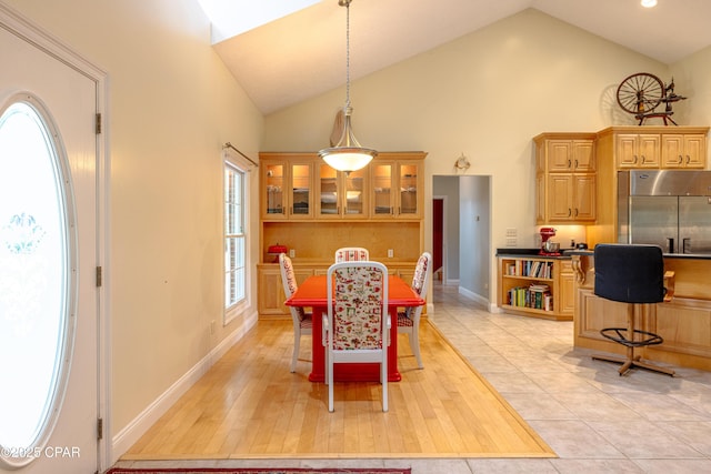 dining space featuring high vaulted ceiling, baseboards, and light wood-style flooring