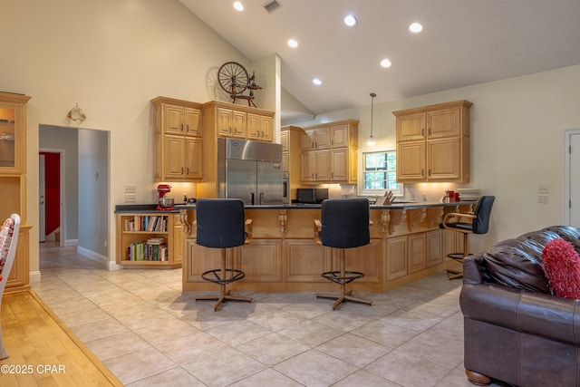 kitchen featuring dark countertops, black microwave, high vaulted ceiling, a kitchen bar, and built in refrigerator
