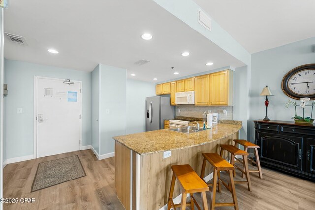 17739 Front Beach Rd Unit 1207W, Panama City Beach, FL 32413 - kitchen with a peninsula, light wood finished floors, light brown cabinets, stainless steel fridge with ice dispenser, and white microwave