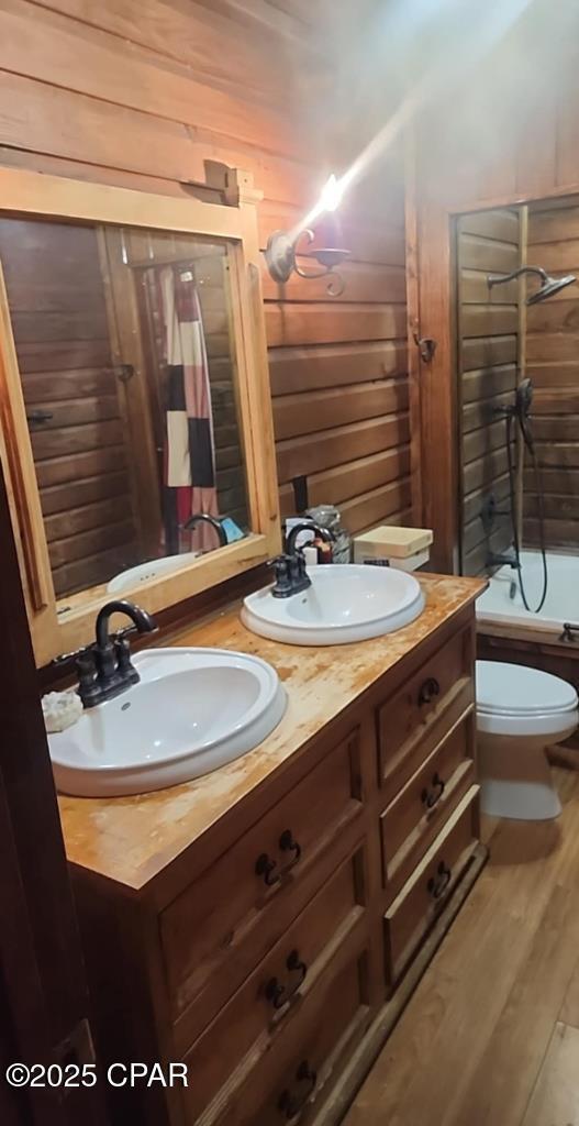bathroom with shower / bath combo with shower curtain, a sink, wooden walls, and toilet
