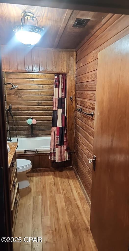 full bath featuring vanity, wood walls, wood finished floors, toilet, and shower / bathtub combination with curtain