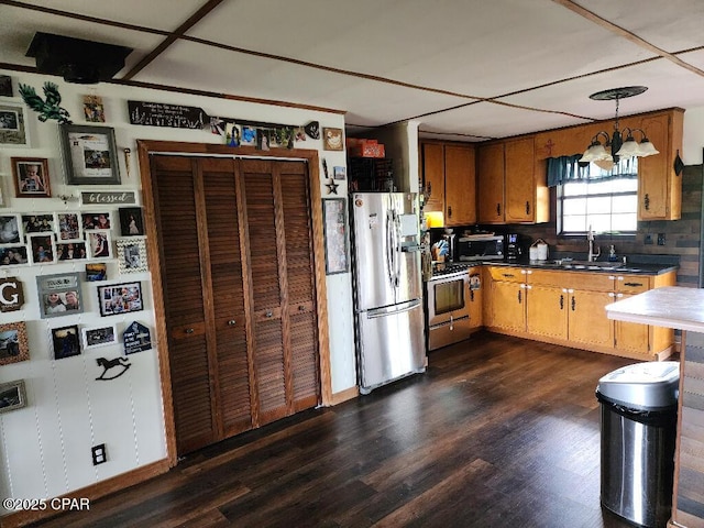 kitchen with dark wood-style flooring, dark countertops, a sink, a chandelier, and stainless steel appliances