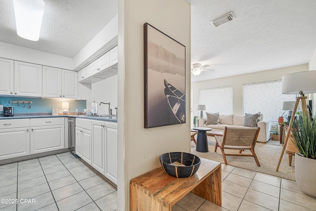 kitchen with a textured ceiling, light tile patterned flooring, white cabinets, open floor plan, and a sink