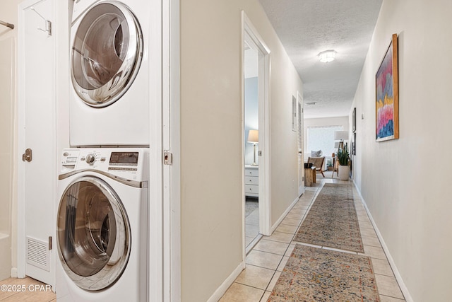 laundry area with stacked washer and clothes dryer, a textured ceiling, light tile patterned floors, and baseboards