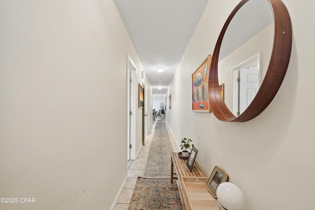 corridor featuring light tile patterned floors, a textured ceiling, and baseboards