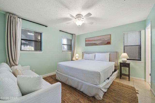 bedroom with a textured ceiling, baseboards, ceiling fan, and light tile patterned flooring