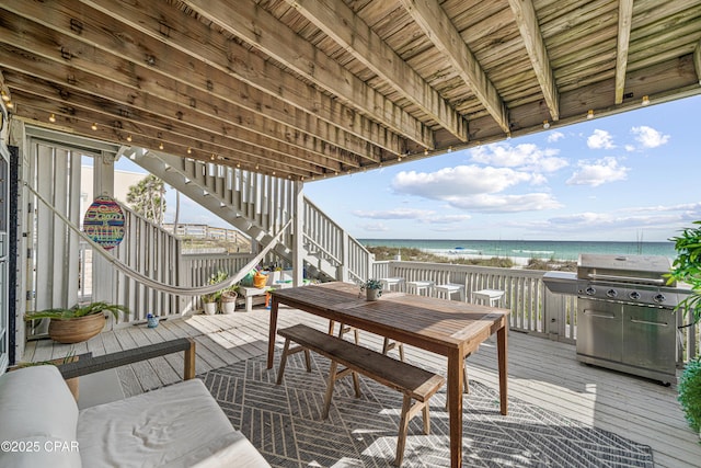wooden deck with stairs, grilling area, view of water and beach, and outdoor dining space