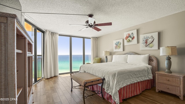 bedroom featuring a water view, access to exterior, multiple windows, expansive windows, and wood finished floors