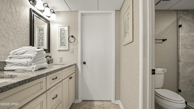bathroom with a textured wall, toilet, double vanity, and tile patterned flooring