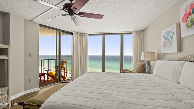 bedroom with access to exterior, a water view, wood finished floors, multiple windows, and a textured ceiling